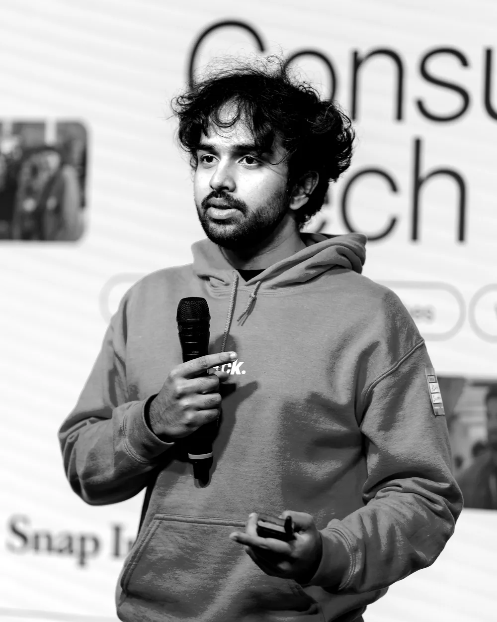 Ashwin on stage, mid-sentence, a microphone in one hand and a clicker in the other.